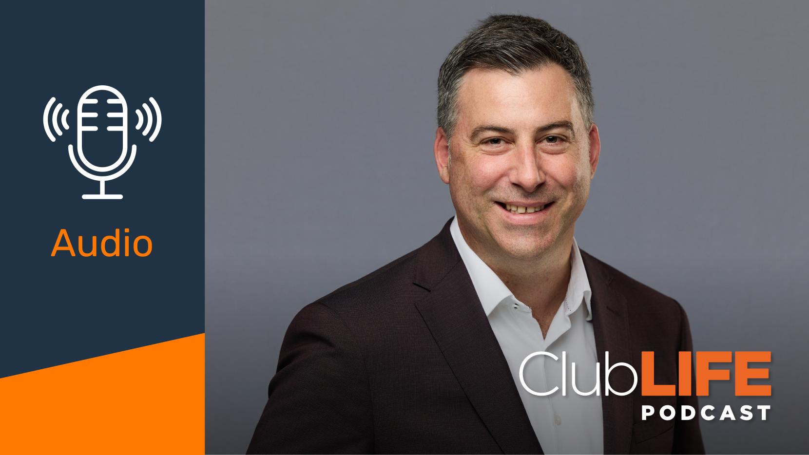 A smiling man in a suit with 'ClubLIFE Podcast' and 'Audio' overlays on a gray background.