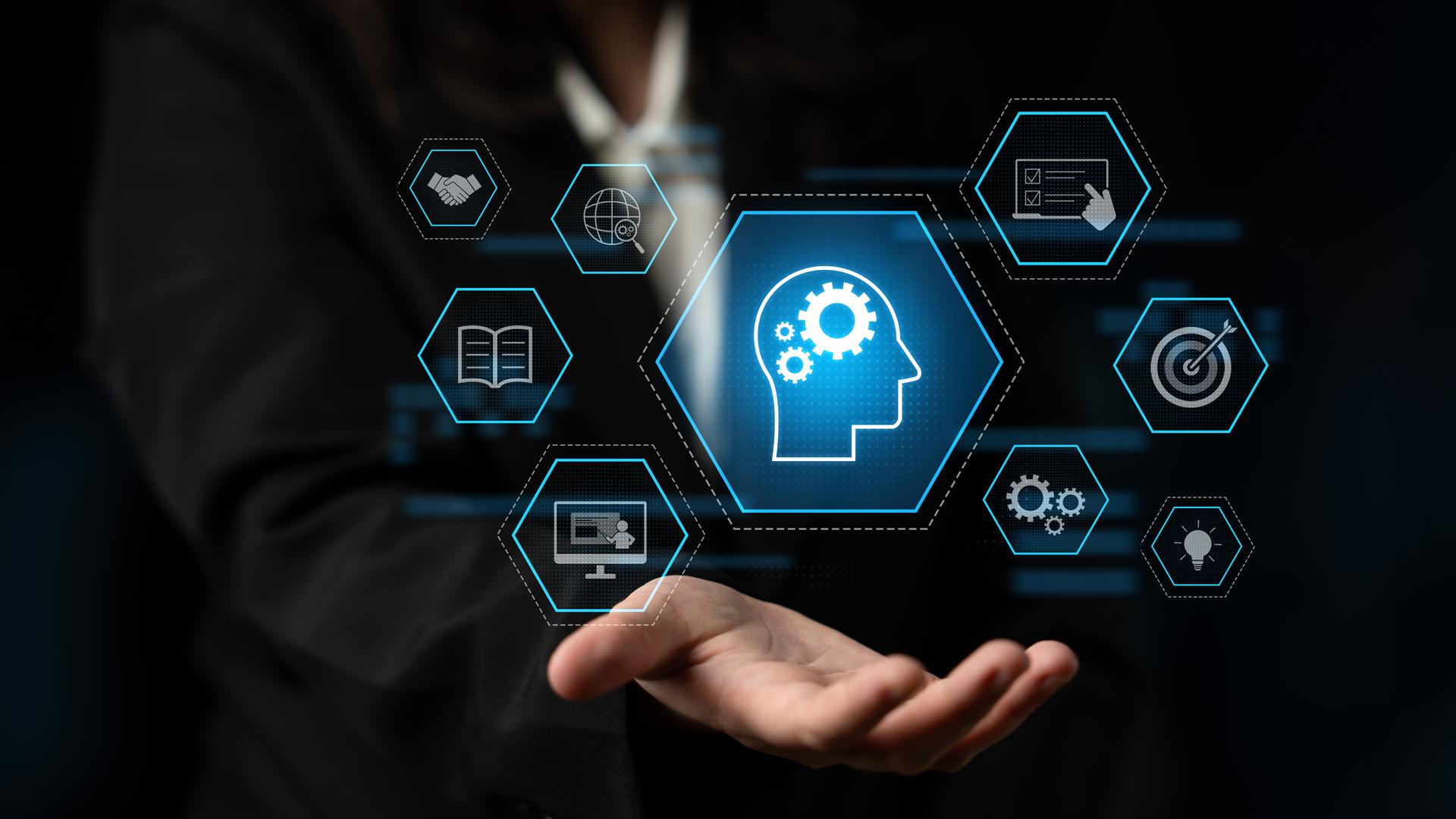 A person in a suit holds out their hand, above which a holographic display of interconnected hexagonal icons floats. The central icon is a human head with gears inside, surrounded by symbols for handshake, global search, book, computer, checklist, target, gears, and lightbulb.