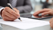 Close-up of a hand holding a fountain pen, writing on a document with printed text.
