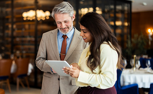 Two business people, a man and a woman, looking at a tablet in a restaurant setting.